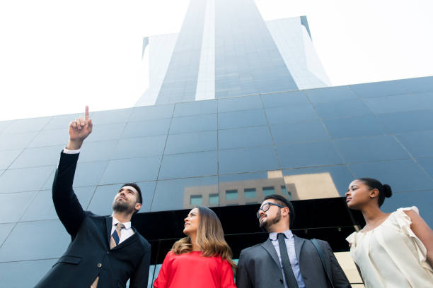 A multi-ethnic group of business partners following directions from their team leader in front of a large building